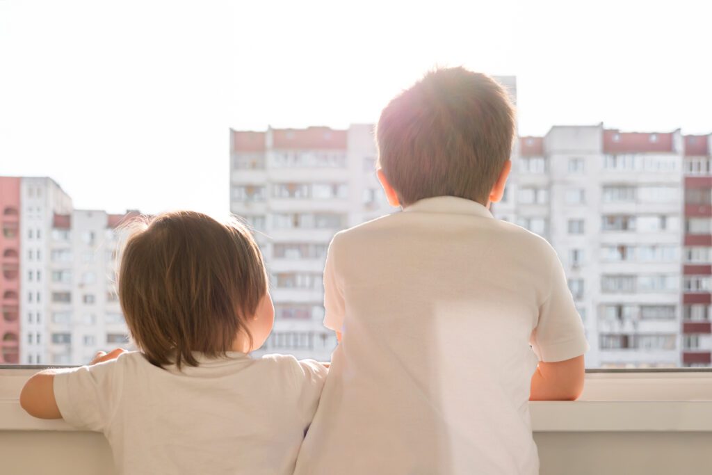 Två barn står på en balkong och tittar ut över ett bostadsområde
